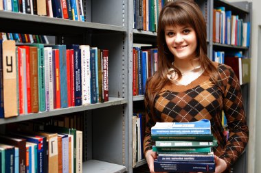 The young nice student reads and considers books on regiments in the big library, smiling in the chamber clipart