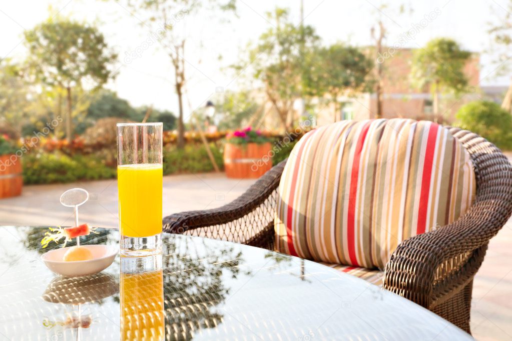Glass of orange juice and ice cream on table in a garden.