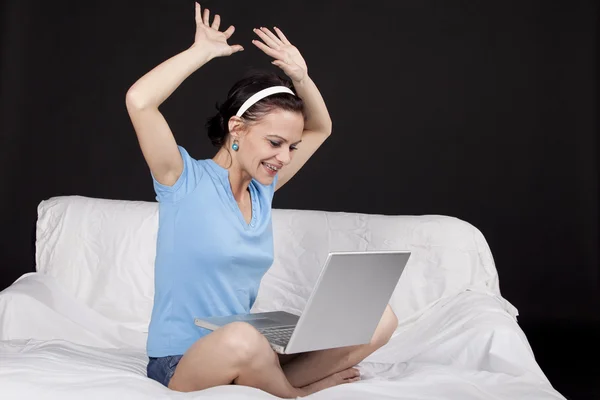 Ganska ung kvinna sitter på sängen med sin laptop — Stockfoto