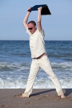 Sunburnt businessman at the beach throwing his laptop. Concept of protesting against work on vacation clipart