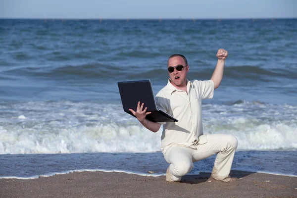 Злой человек бьет ноутбук на пляже — стоковое фото
