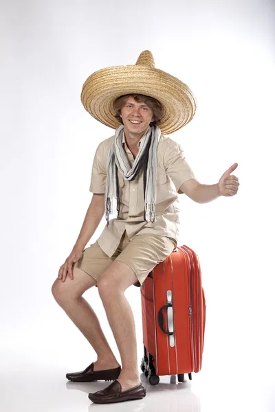 stock image Smiling young mexican man with sombrero hitchhiking and sitting on his luggage