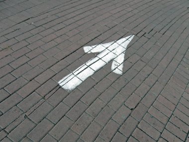 Painted white direction sign over brick road, transportation. clipart