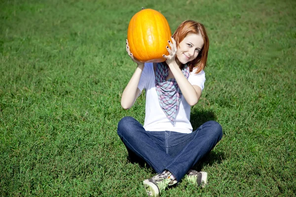 若い女性の緑の芝生に座っているとカボチャを維持します。. — ストック写真
