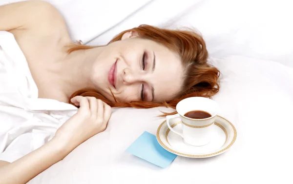 Frau in Weiß liegt im Bett neben Tasse Kaffee. — Stockfoto
