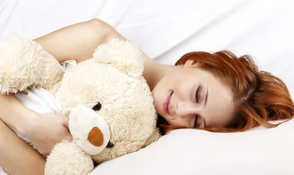 Frau im weißen Nachthemd liegt mit Stofftier im Bett. — Stockfoto