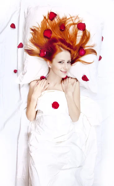 Vacker rödhårig flicka i sängen med rosenblad. — Stockfoto