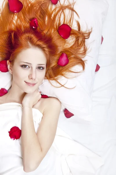 Schöne rothaarige Mädchen im Bett mit Rosenblatt. — Stockfoto