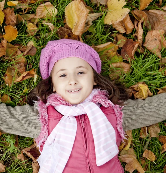 Lying down little girl at grass and leafs in the park. — Stock Photo, Image