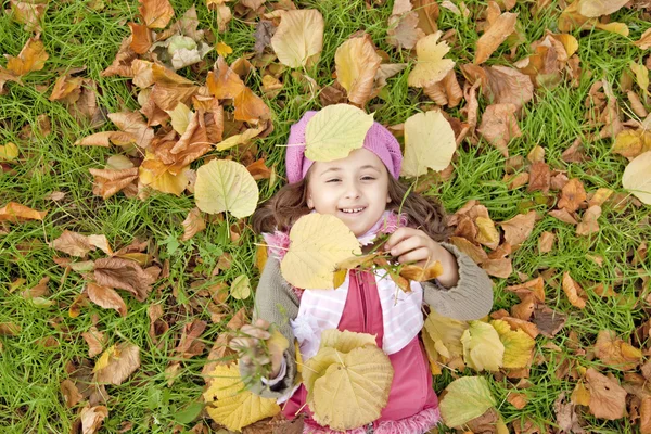 Vleže se děvčátko v trávě a listí v parku. — Stock fotografie