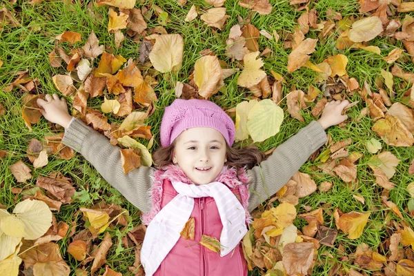 Kłamliwy w dół dziewczynka w trawy i liści w parku. — Zdjęcie stockowe