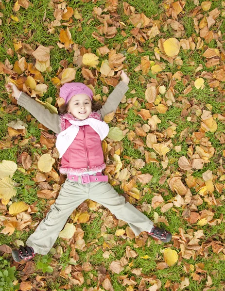 Liegen kleines Mädchen auf Gras und Blättern im Park. — Stockfoto