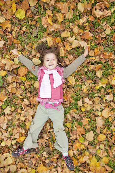 Lying down little girl at grass and leafs in the park. — Stock Photo, Image