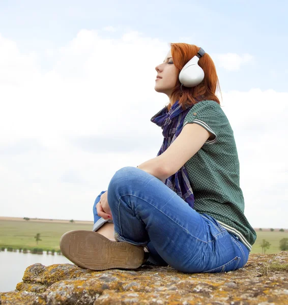 Ung flicka med hörlurar på gräs i vår tid. — Stockfoto