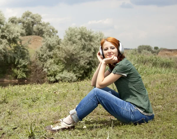年轻时尚女孩用耳机在草的春天. — 图库照片