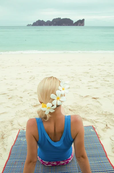 Närbild av kvinna sittplatser på stranden med blommor i håret ser till havet — Stockfoto