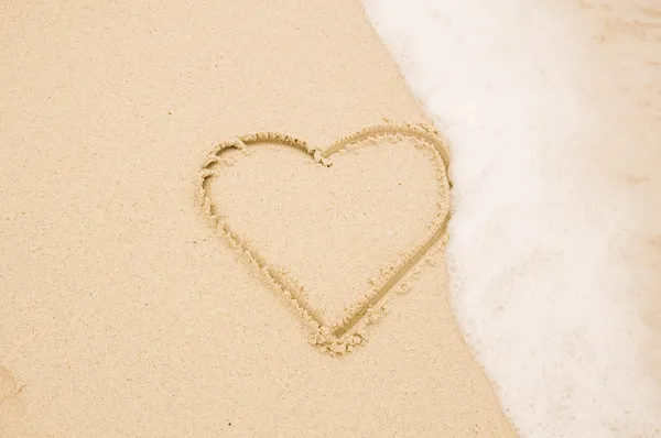 Corazón escrito a mano en la arena con la onda approachin — Foto de Stock