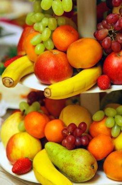 Assorted fresh fruit including bananas, tangerines, apples, grapes and pears sitting in a plate clipart
