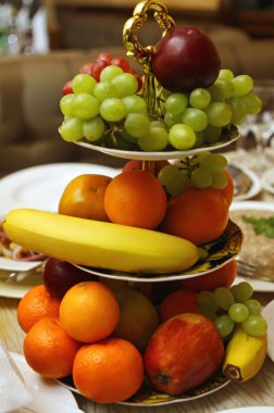 Assorted fresh fruit including bananas, tangerines, apples, grapes and pears sitting in a plate clipart