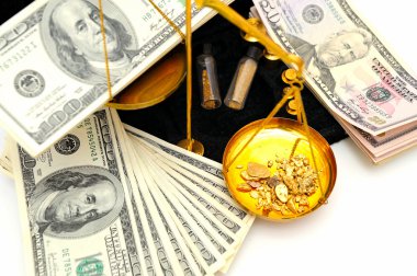 Gold nuggets in the pan of a balance scale with many fifty and hundred dollar bills showing the value of both clipart