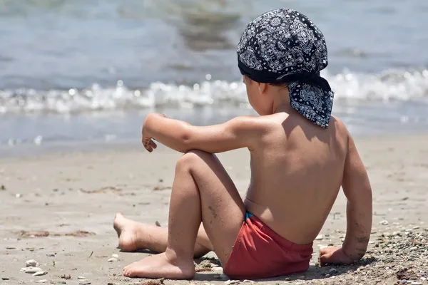 Mały chłopiec siedzi na plaży — Zdjęcie stockowe