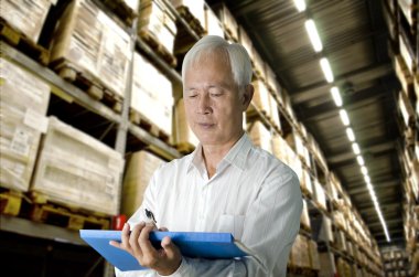 Senior asian business man doing stock count in a warehouse clipart