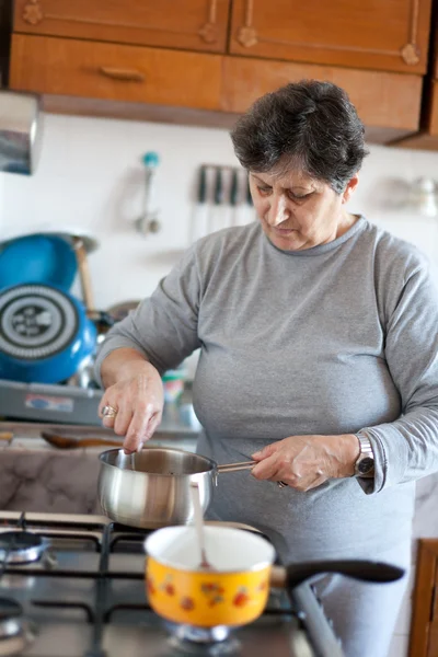 明るい日光の下でストーブの上調理する年配の女性 — ストック写真