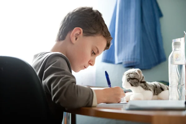 彼は机に向かって宿題をやっている少年 — ストック写真