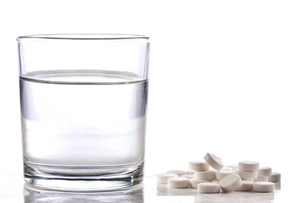 Білі таблетки зі склянкою води — стокове фото