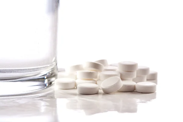 白い背景で隔離の水のガラスの近く白い錠剤の山 — ストック写真