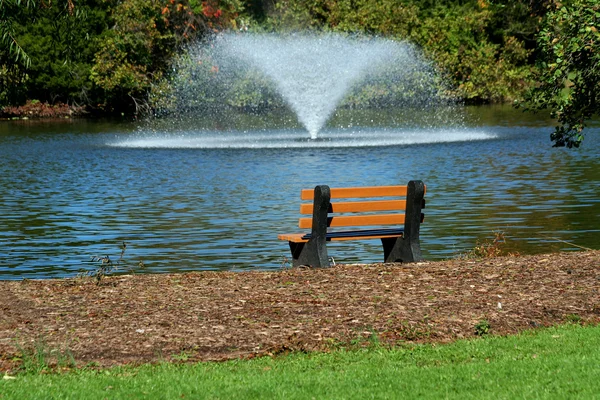 Фонтан на пруду со скамейкой в парке — стоковое фото