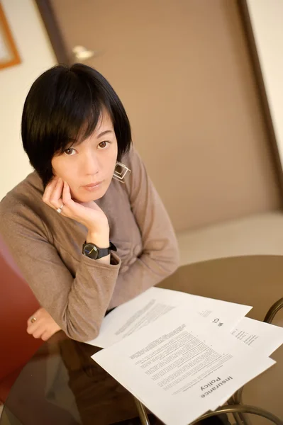 亚洲女人阅读在办公室桌上的保险政策文件 — 图库照片
