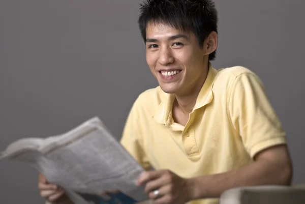 Счастливый Улыбающийся Молодой Человек Азии Сидит Читает Газету Сером Фоне — стоковое фото
