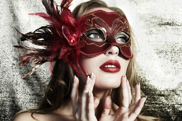Beautiful young woman in a red mysterious venetian mask on a gold backgroun Stock Photo