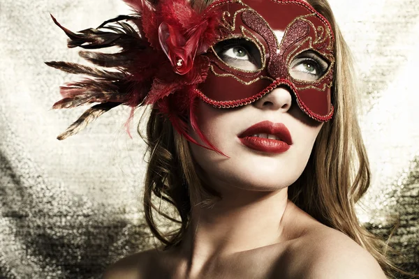 Beautiful young woman in a red mysterious venetian mask on a gold backgroun Stock Photo