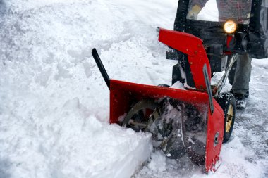 Winter season fun: Man removing snowstorm aftermath with a bright red snowblower. clipart