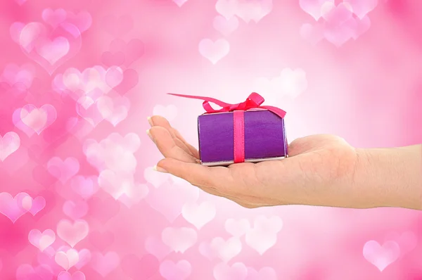 Weibliche Hand hält lila Geschenk auf rosa Herz Hintergrund — Stockfoto