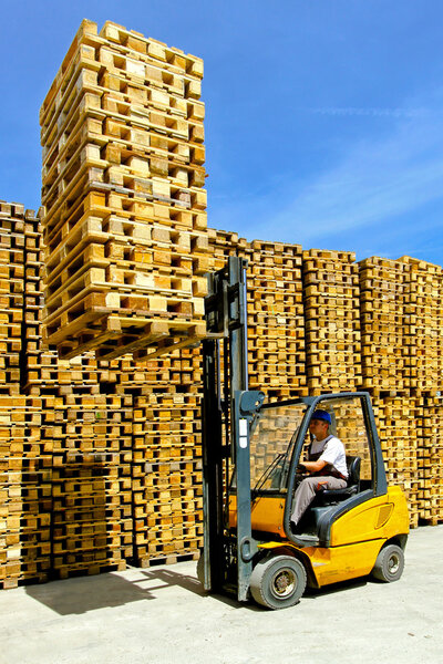 Man operating forklift lifting bunch of euro pallets