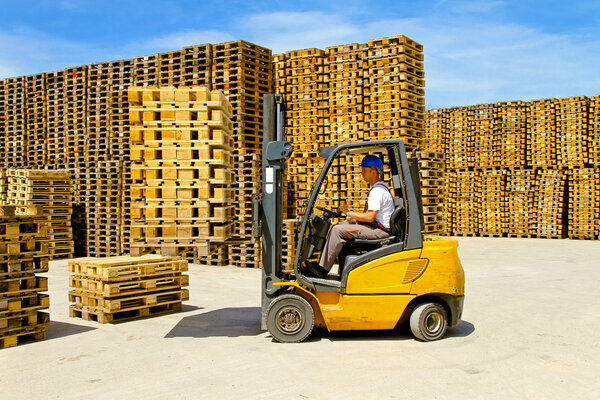 Forklift operator handling wooden pallets in warehouse