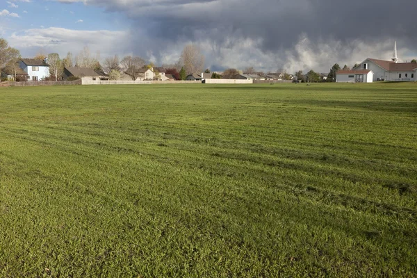 住宅の家 バック グラウンドで重い嵐雲を持つ草の新たに刈られた 大規模なフィールド — ストック写真