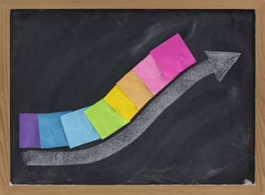 Growth, progress or success concept presented with thick white chalk arrow and colorful blank sticky notes on blackboard, eraser smudges