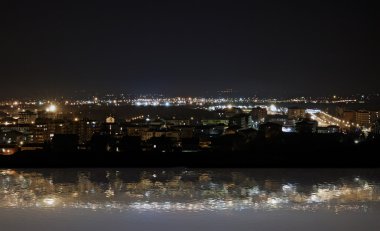 sudaki yansıması ile güneş battıktan sonra yanan bir şehir manzarası