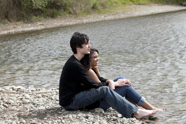 Adolescente casal sentado na margem do rio pedregoso — Fotografia de Stock