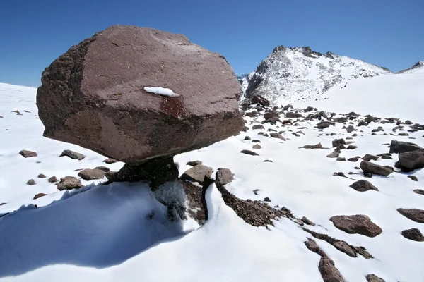 Huge stone in form mushroom against snow mountains — Stock Photo, Image