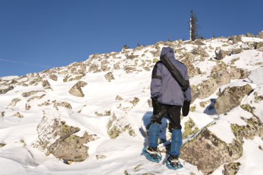 Climber in snowshoes (snow shoes) walking at the mountain slope. Russia. Ur clipart