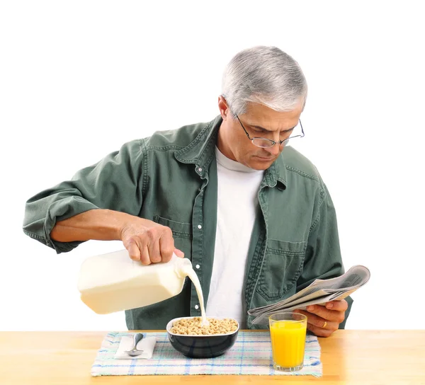 Мужчина средних лет наливает молоко в миску с зерном — стоковое фото