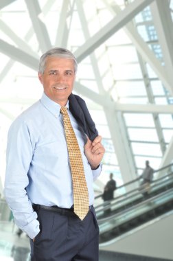 Middle aged businessman standing in front of an escalator with his jacket slung over his shoulder. Vertical format. clipart