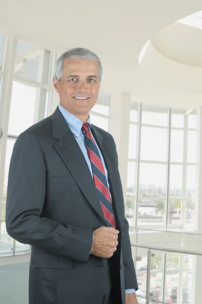 近代的なオフィス ロビーに立って中央高齢者のビジネスマン カメラに向かって笑みを浮かべて男と垂直方向の形式 — ストック写真