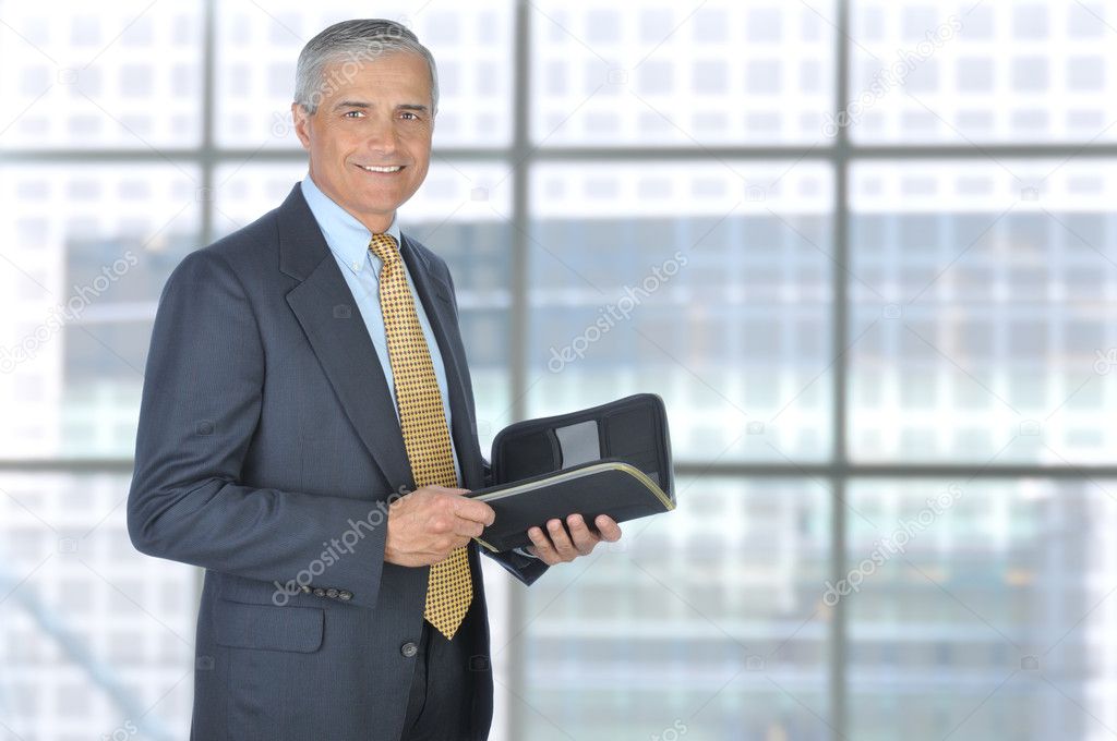 Standing Middle Aged Businessman with Planner Notebook in Modern Office Setting, Horizontal Format.