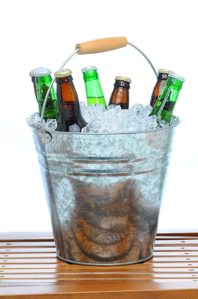 各種ボトル 白い背景の前でチーク材のテーブルの上の氷で満ちているビールのバケツ — ストック写真